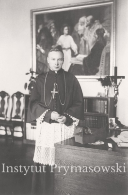 Bp. S. Wyszynski i w swoim gabinecie,  stoi obok biurka na tle duzego obrazu ( 12- letni P.Jezus w swiatyni ).