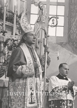 Bp. S. Wyszynski w stroju liturgicznym stoi na tle oltarza. Obok  ks. NN.