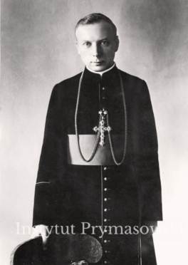 Zdjecie portretowe .Bp S.Wyszynski stoi.Postac do kolan. .Prawa reke opierta o oparcie krzesla.