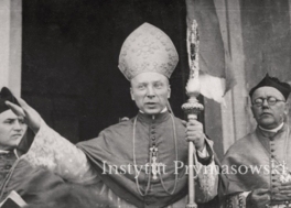 Przemawiajacy bp.S. Wyszynski (w mitrze i z pastoralem) obok dwoch asystujacych  ksiezy.